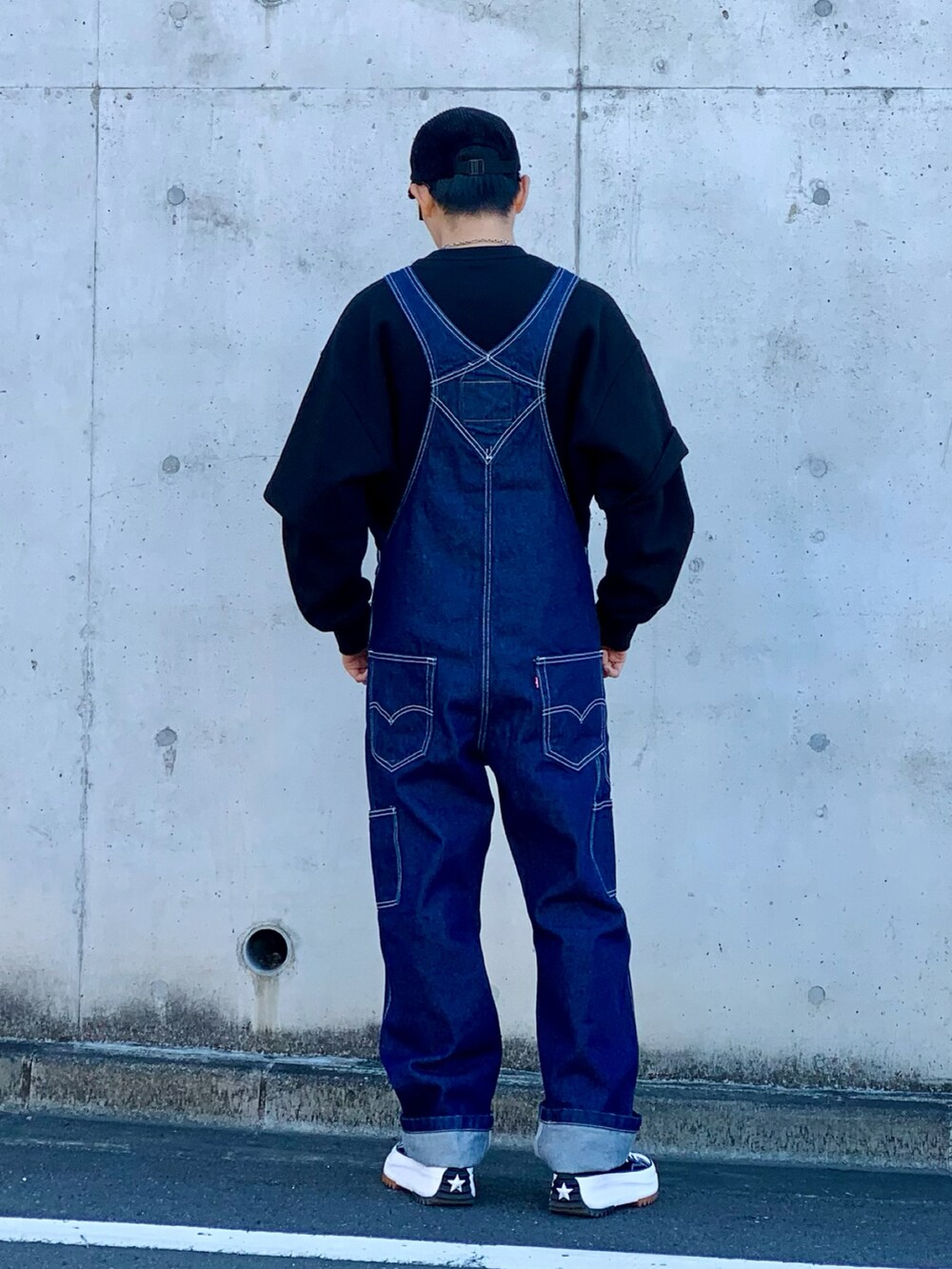 ブラック系のスウェット、ブルー系のサロペット/オーバーオール、ブラック系のスニーカーを着用したメンズの春コーディネートの3枚目の写真