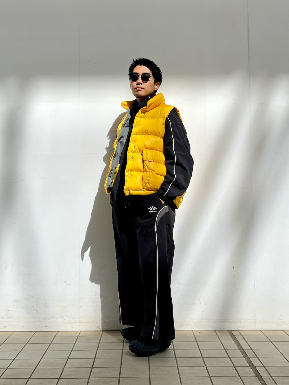 イエロー系のダウンベスト、ブラック系のナイロンジャケット、ブラック系のその他パンツを着用したメンズの春コーディネートの2枚目の写真