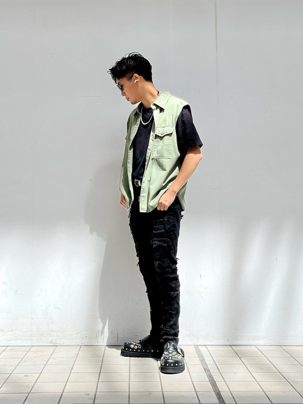 グリーン系のベスト、ブラック系のデニムパンツ、ブラック系のサンダルを着用したメンズの秋コーディネートの2枚目の写真