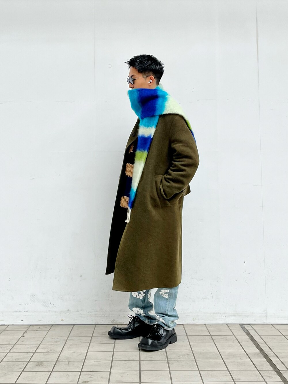 グリーン系のステンカラーコート、ブルー系のニット/セーター、ブルー系のデニムパンツを着用したメンズの冬コーディネートの2枚目の写真