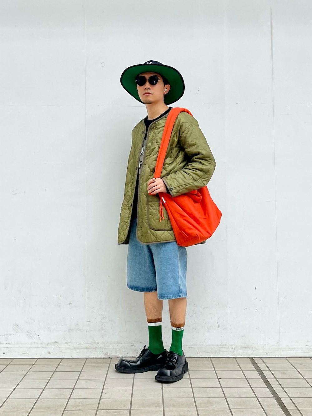 グリーン系のモッズコート、ブルー系のデニムパンツ、オレンジ系のバッグを着用したメンズの春コーディネートの2枚目の写真