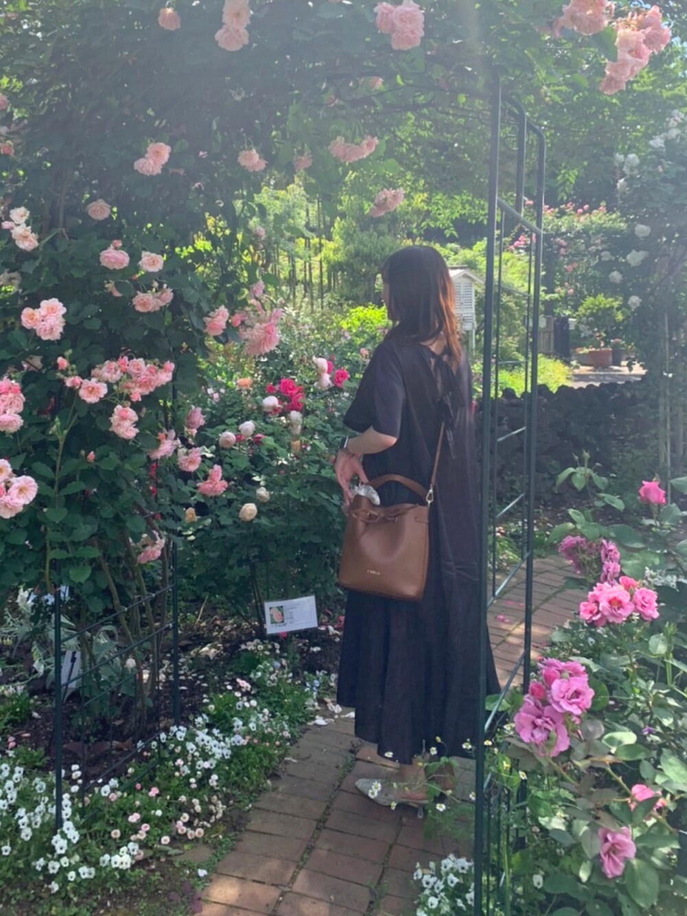 ブラウン系のショルダーバッグ、ブラック系のワンピース、グリーン系のパンプスを着用したレディースの春コーディネートの2枚目の写真