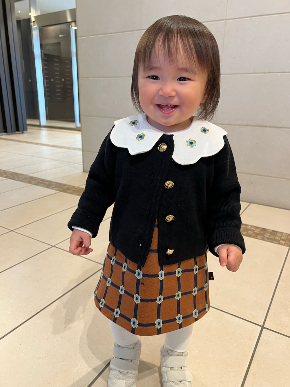 ブラック系のカーディガン/ボレロ、ブラウン系のワンピース、ホワイト系のスニーカーを着用したキッズの秋コーディネートの3枚目の写真