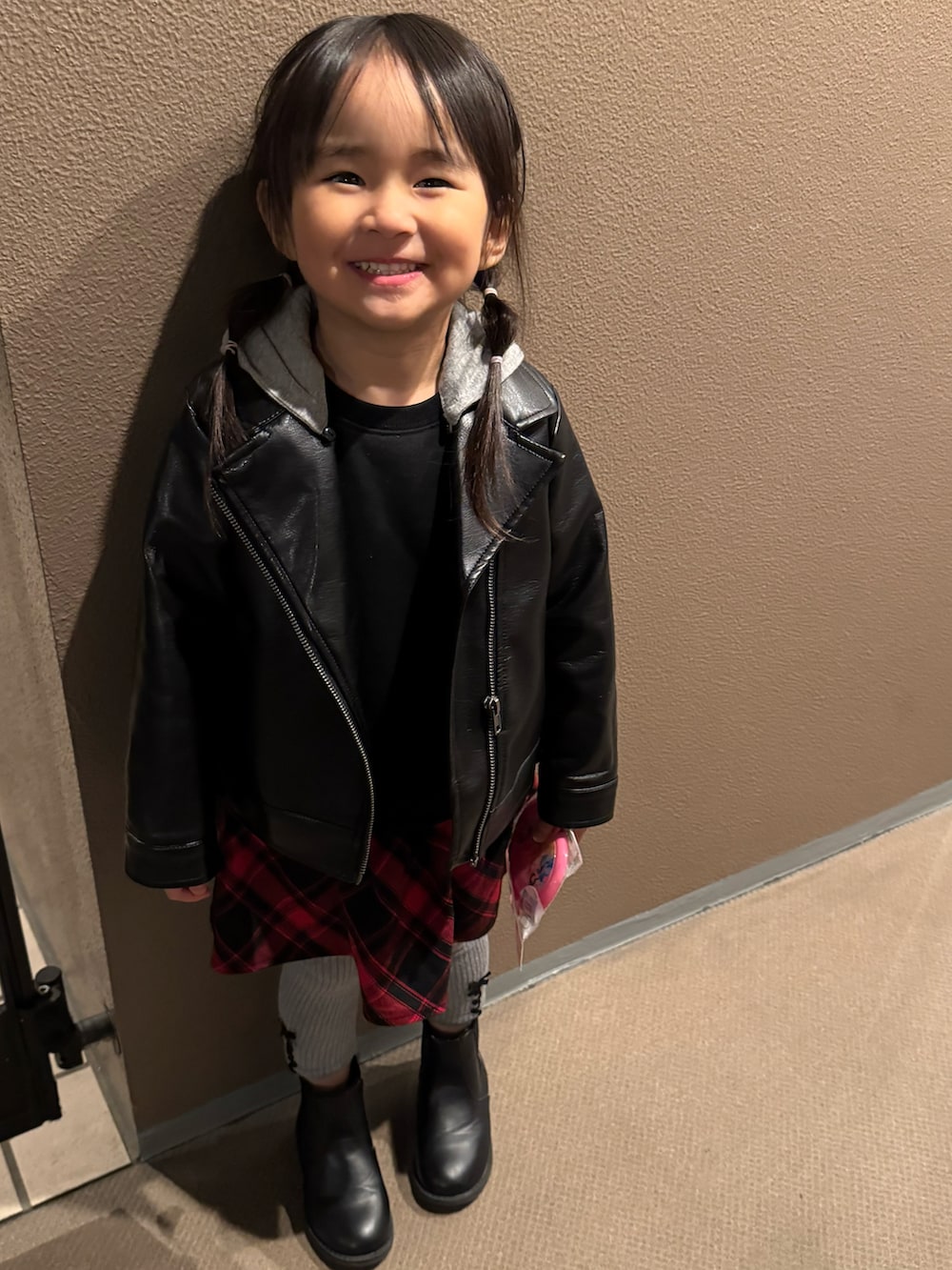 ブラック系のブーツ、ブラック系のライダースジャケット、レッド系のワンピースを着用したキッズの冬コーディネートの2枚目の写真