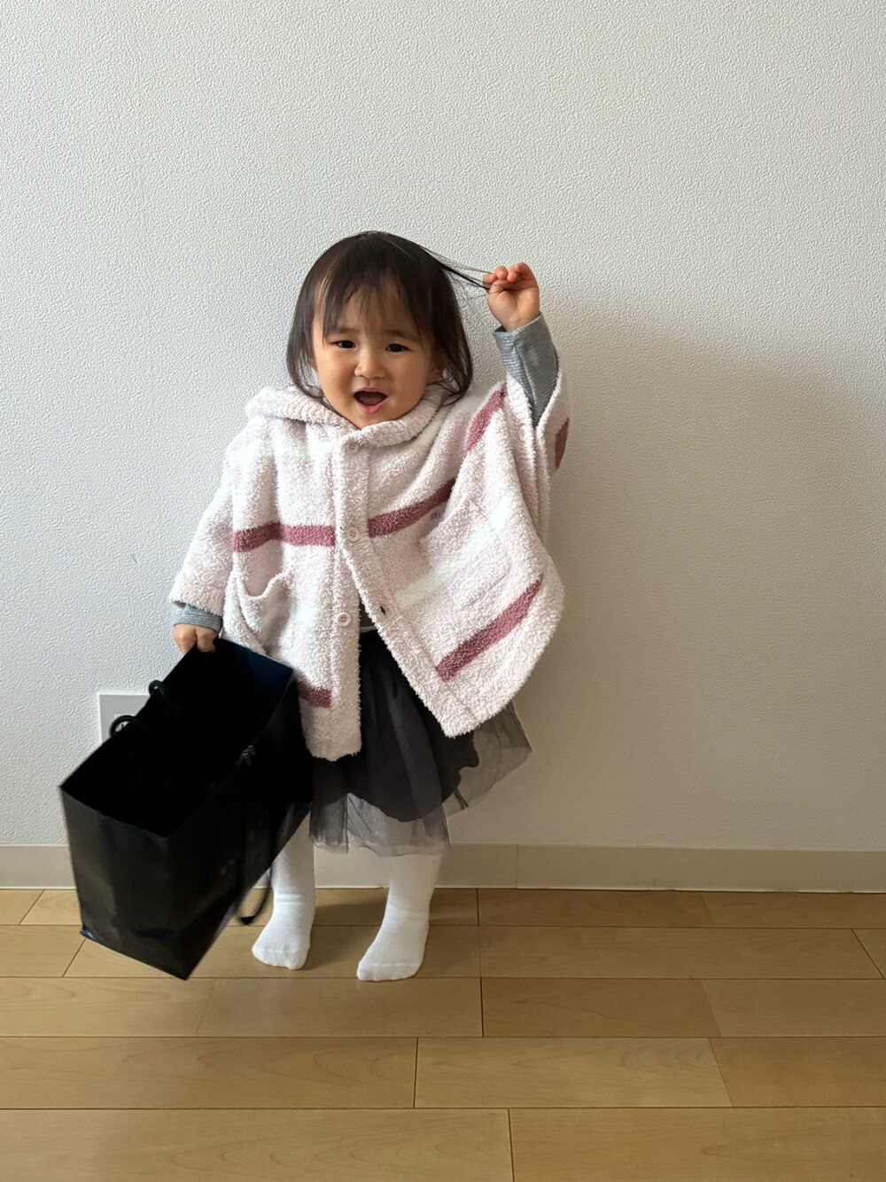 ピンク系のポンチョ、グレー系のTシャツ/カットソー、グレー系のスカートを着用したキッズの冬コーディネートの2枚目の写真