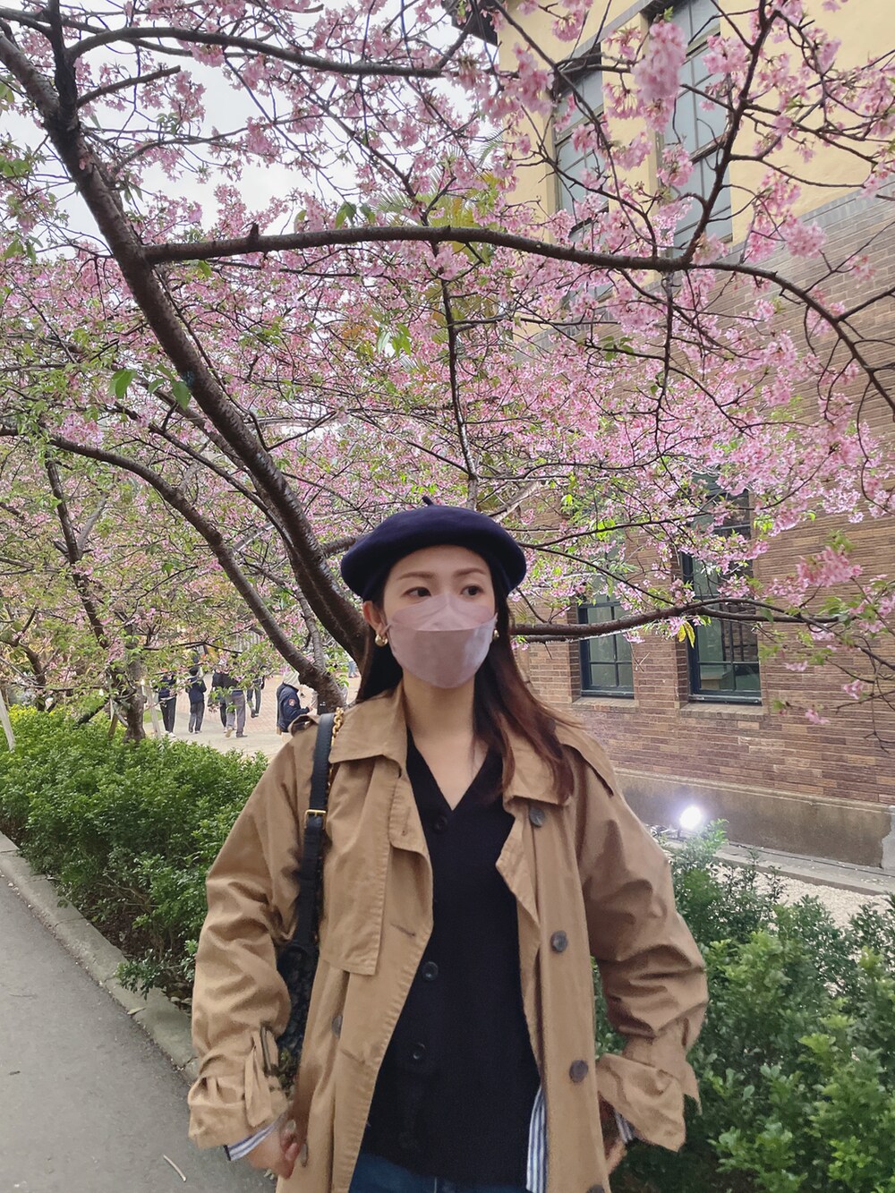 ベージュ系のトレンチコート、ブラック系のスニーカー、ブルー系のハンドバッグを着用したレディースの春コーディネートの2枚目の写真