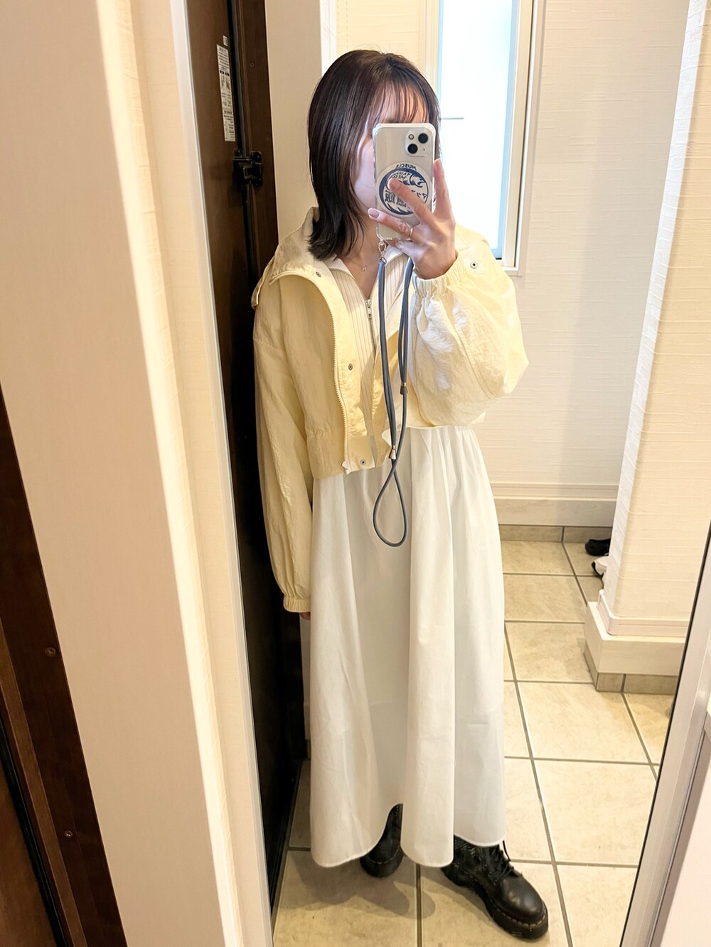 ブラック系のブーツ、ホワイト系のワンピース、ホワイト系のマウンテンパーカーを着用したレディースの春コーディネートの2枚目の写真