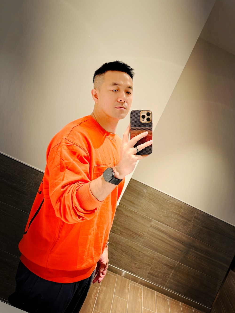 オレンジ系のスウェット、ブラック系のショルダーバッグ、グレー系のチノパンツを着用したメンズの夏コーディネートの2枚目の写真