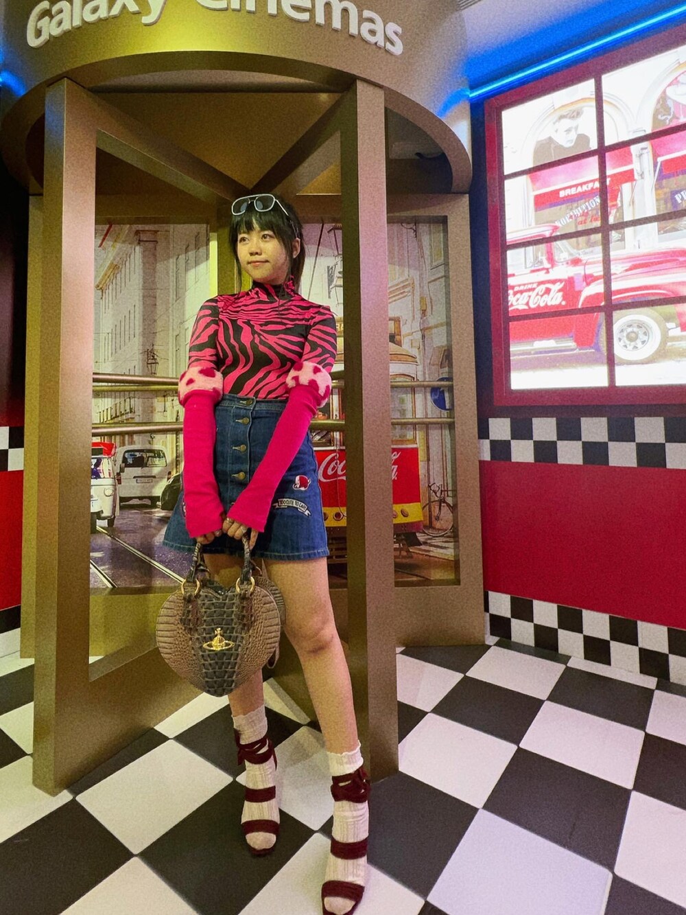 ピンク系のトートバッグ、ブルー系のデニムスカート、ブルー系のサングラスを着用したレディースの夏コーディネートの2枚目の写真