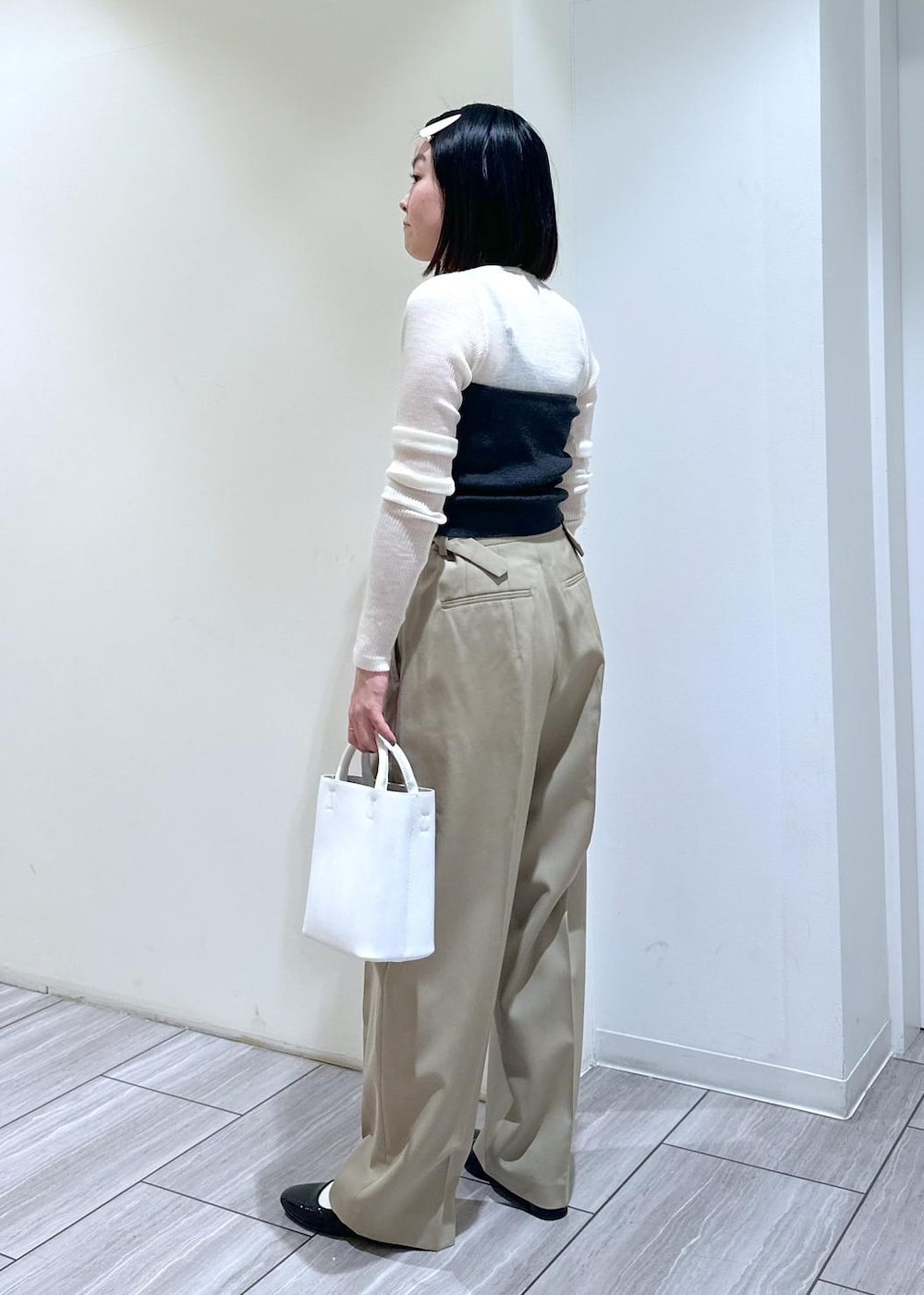 ホワイト系のハンドバッグ、ブラック系のパンプス、ベージュ系のスラックスを着用したレディースの夏コーディネートの2枚目の写真