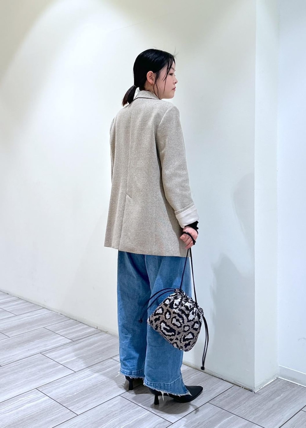 ブルー系のデニムパンツ、ブラック系のブーツ、グレー系のハンドバッグを着用したレディースの秋コーディネートの3枚目の写真