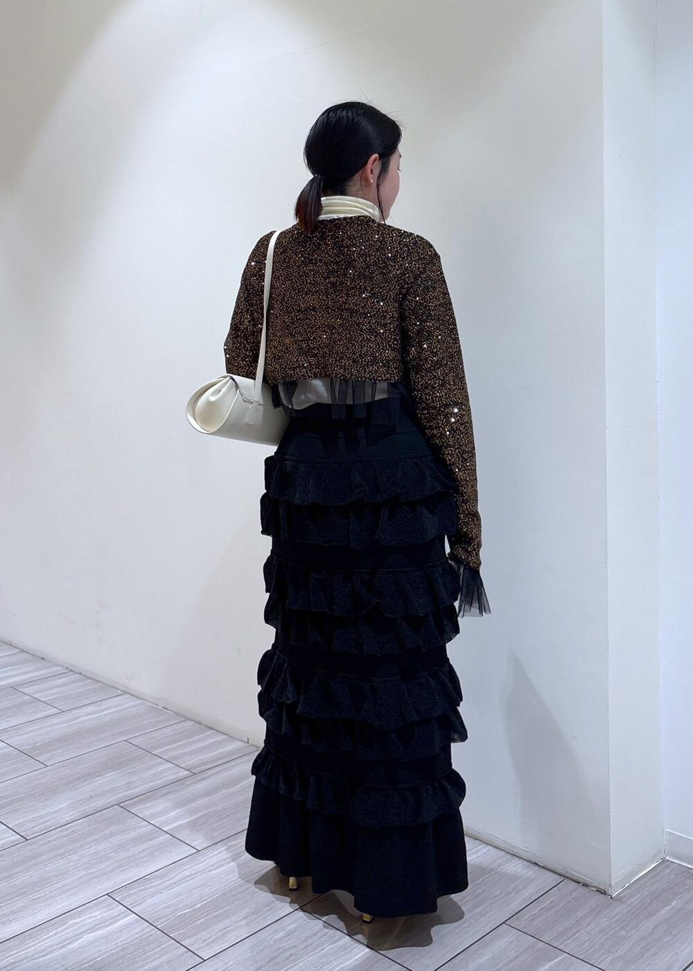 ゴールド系のブーツ、ホワイト系のショルダーバッグ、ブラック系のスカートを着用したレディースの秋コーディネートの3枚目の写真