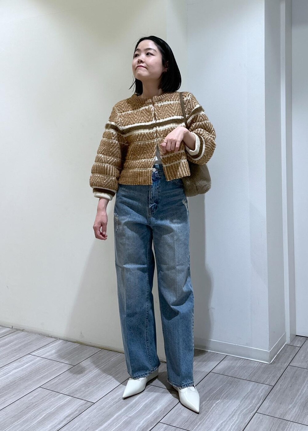 ホワイト系のパンプス、ブルー系のデニムパンツ、ベージュ系のショルダーバッグを着用したレディースの秋コーディネートの2枚目の写真