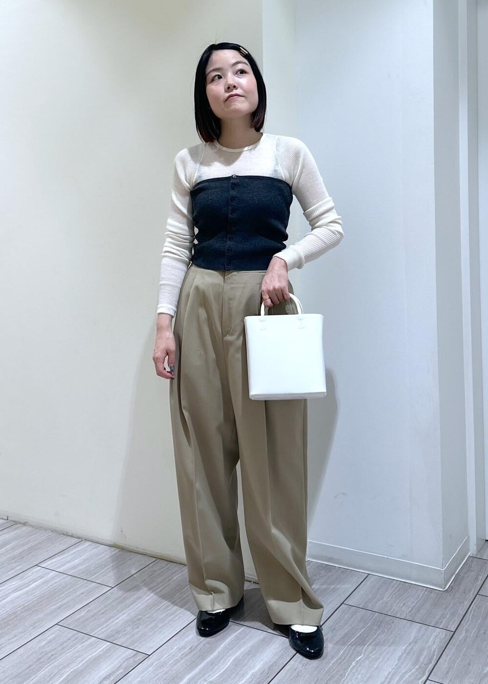 ホワイト系のハンドバッグ、ブラック系のパンプス、ベージュ系のスラックスを着用したレディースの夏コーディネートの4枚目の写真