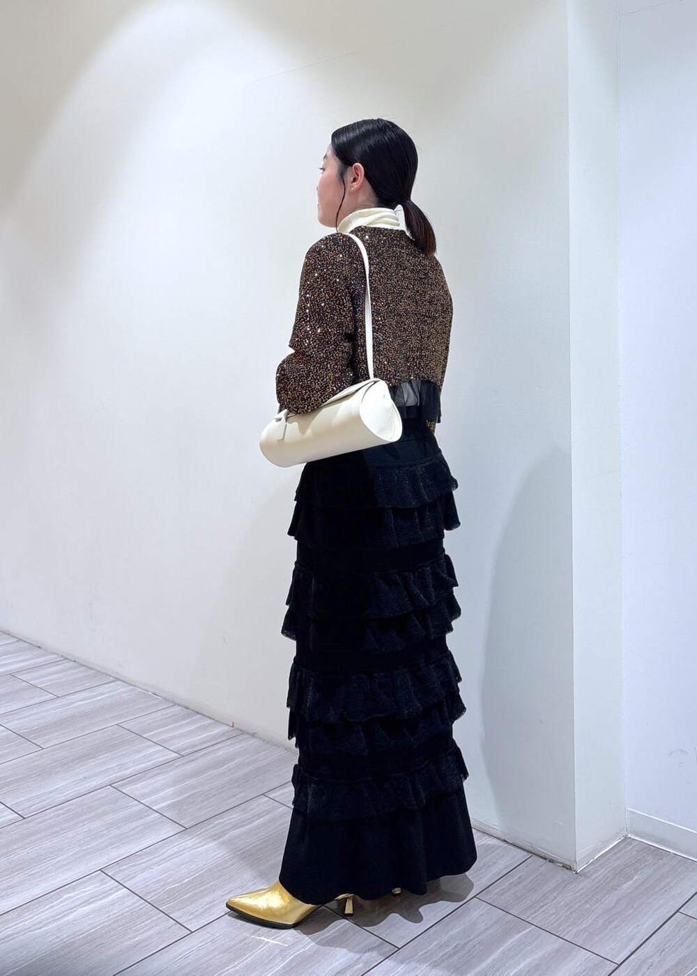 ゴールド系のブーツ、ホワイト系のショルダーバッグ、ブラック系のスカートを着用したレディースの秋コーディネートの2枚目の写真