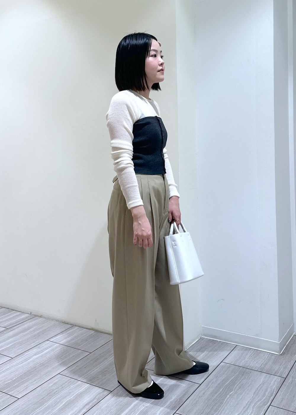 ホワイト系のハンドバッグ、ブラック系のパンプス、ベージュ系のスラックスを着用したレディースの夏コーディネートの3枚目の写真