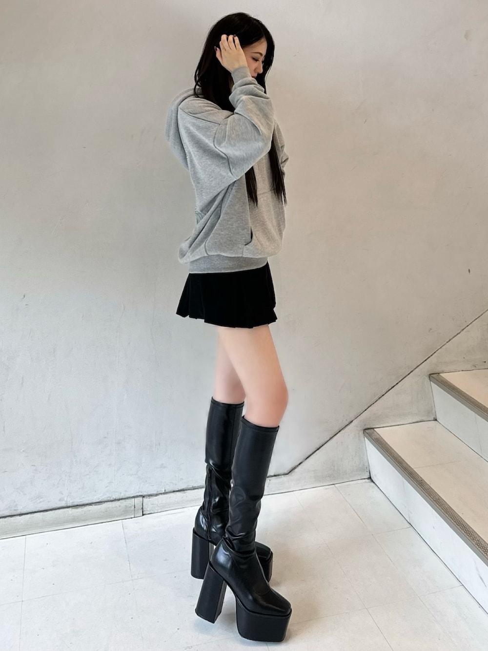 グレー系のパーカー、ブラック系のスカート、ブラック系のブーツを着用したレディースの冬コーディネートの3枚目の写真