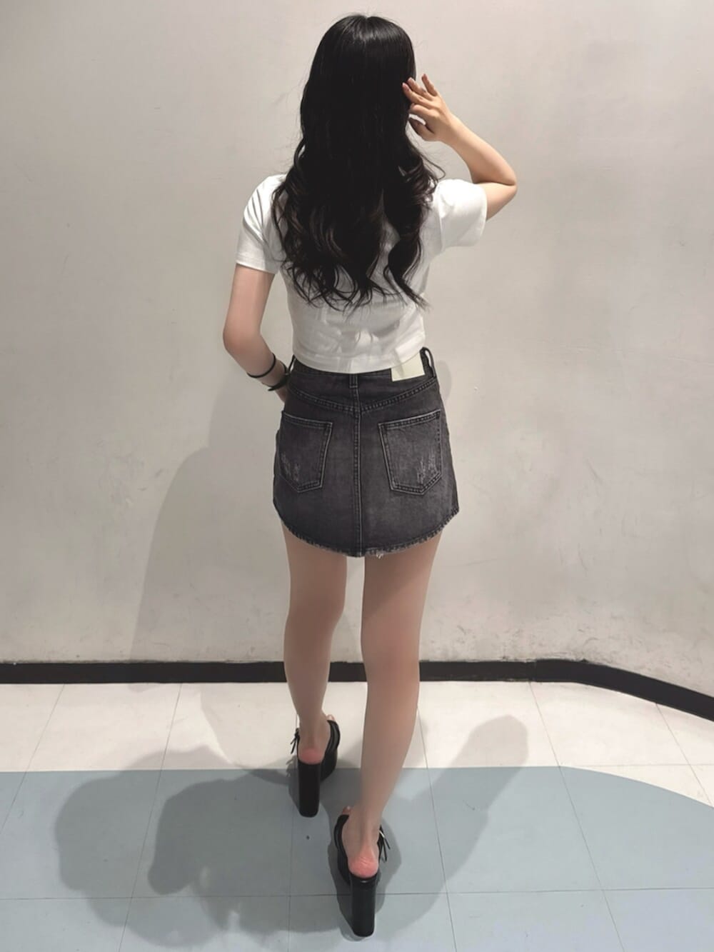 ブラック系のデニムスカート、ホワイト系のTシャツ/カットソー、ブラック系のサンダルを着用したレディースの夏コーディネートの3枚目の写真