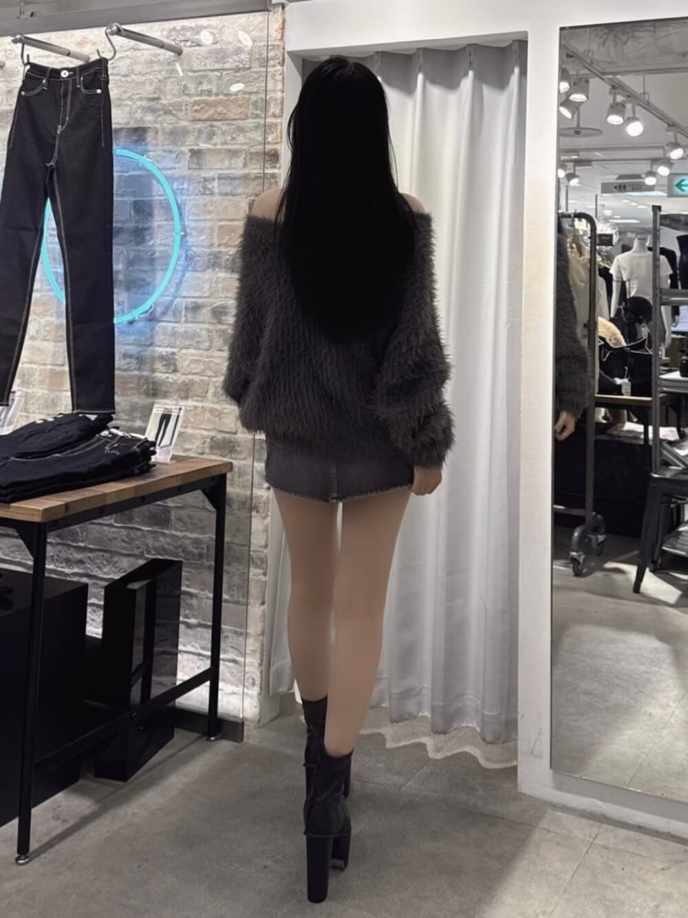 ブラック系のデニムスカート、ブラック系のブーツ、グレー系のニット/セーターを着用したレディースの秋コーディネートの3枚目の写真