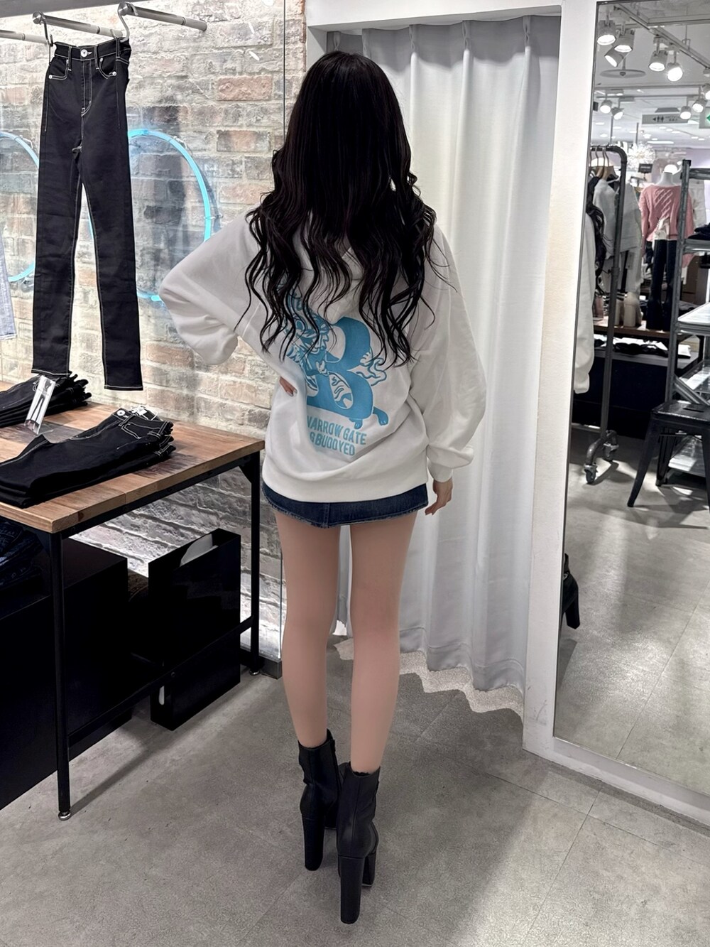 ホワイト系のパーカー、ブラック系のデニムスカート、ブラック系のブーツを着用したレディースの冬コーディネートの2枚目の写真