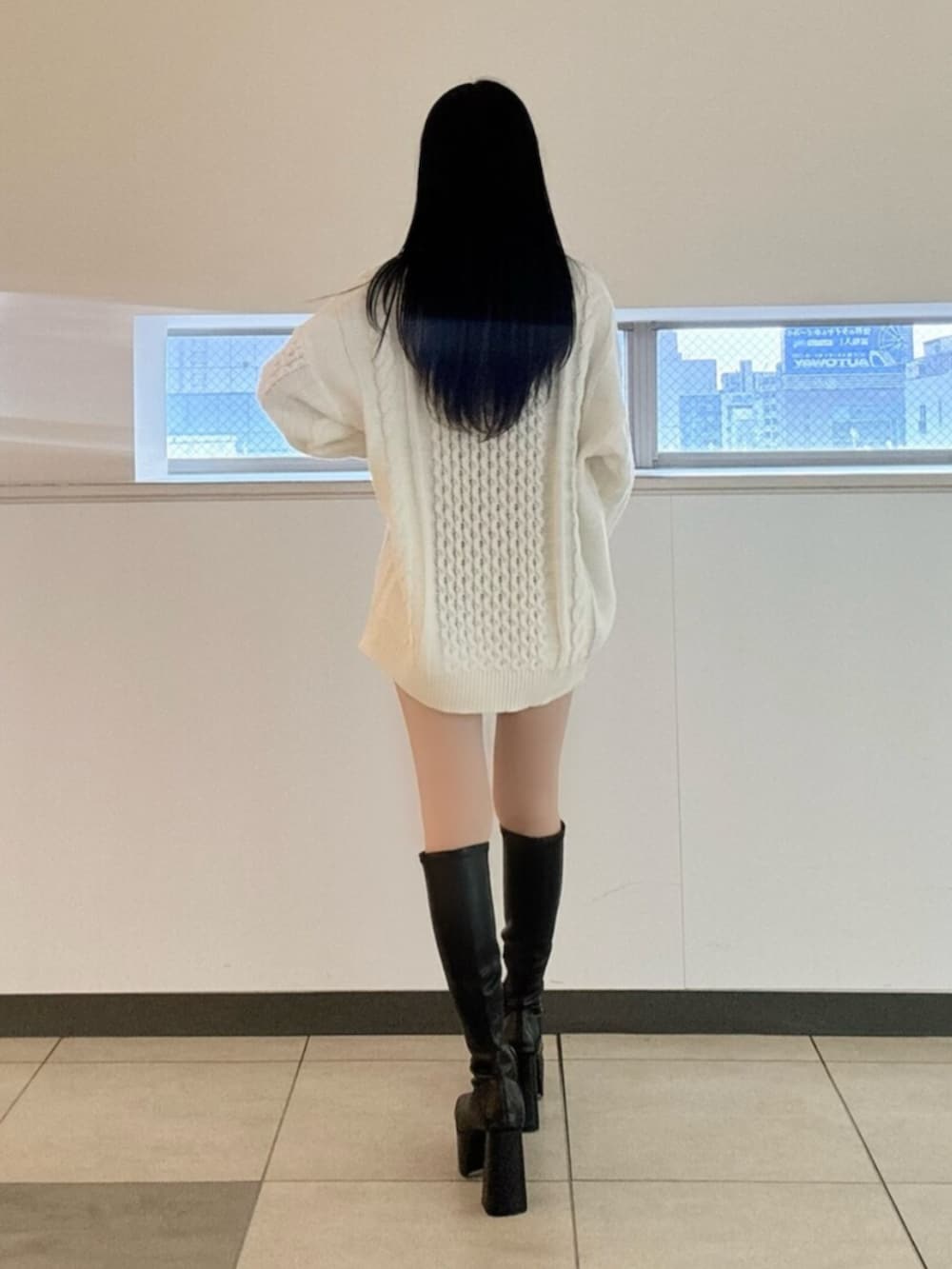 ブラック系のブーツ、ブラック系のデニムスカート、ホワイト系のニット/セーターを着用したレディースの冬コーディネートの2枚目の写真