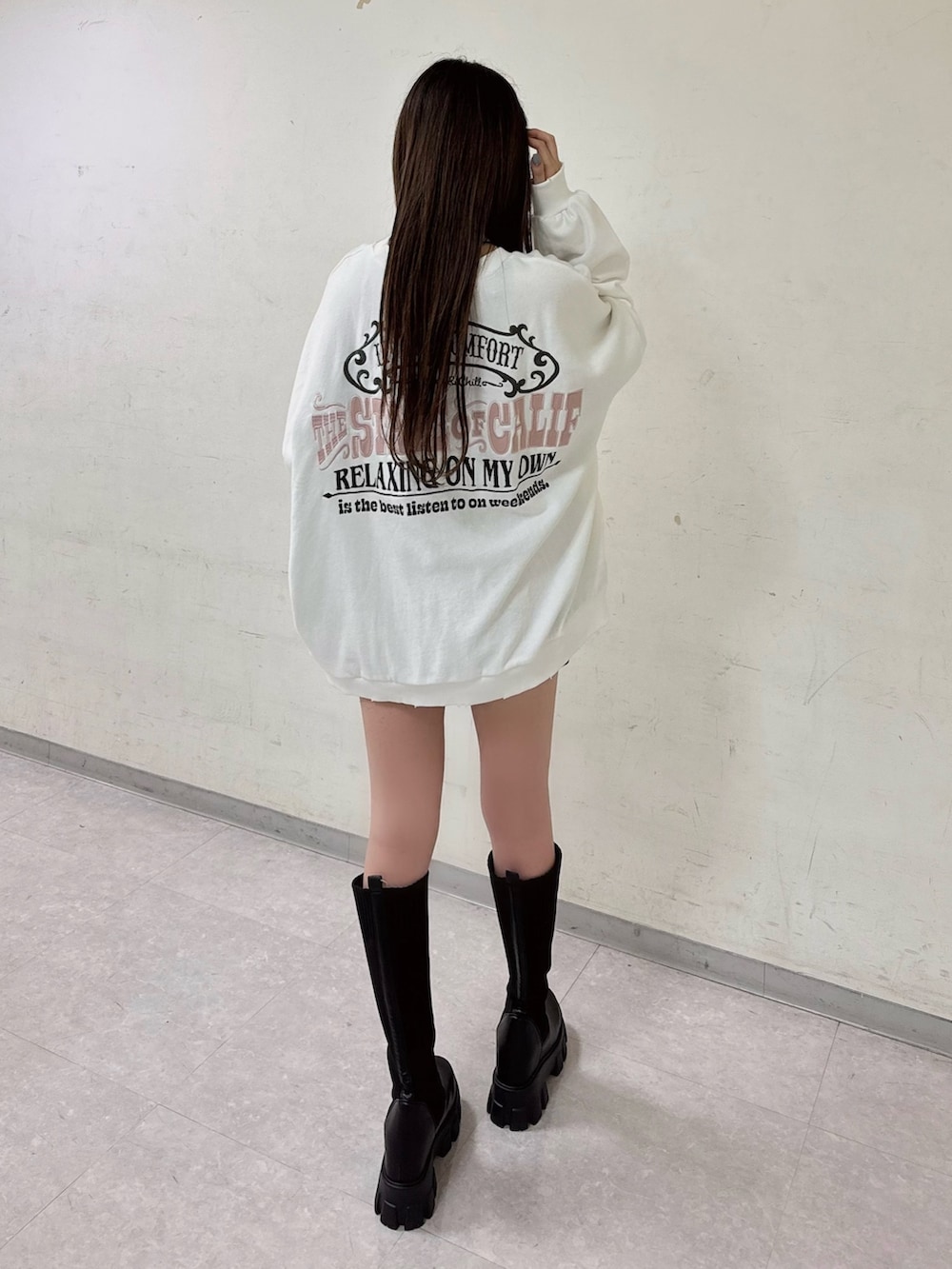 ホワイト系のスウェット、ブラック系のデニムスカート、ブラック系のブーツを着用したレディースの秋コーディネートの3枚目の写真