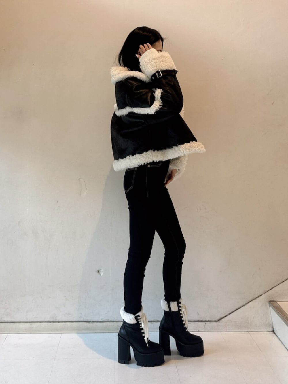 ブラック系のブーツ、ホワイト系のニット/セーター、ブラック系のムートンコートを着用したレディースの冬コーディネートの2枚目の写真