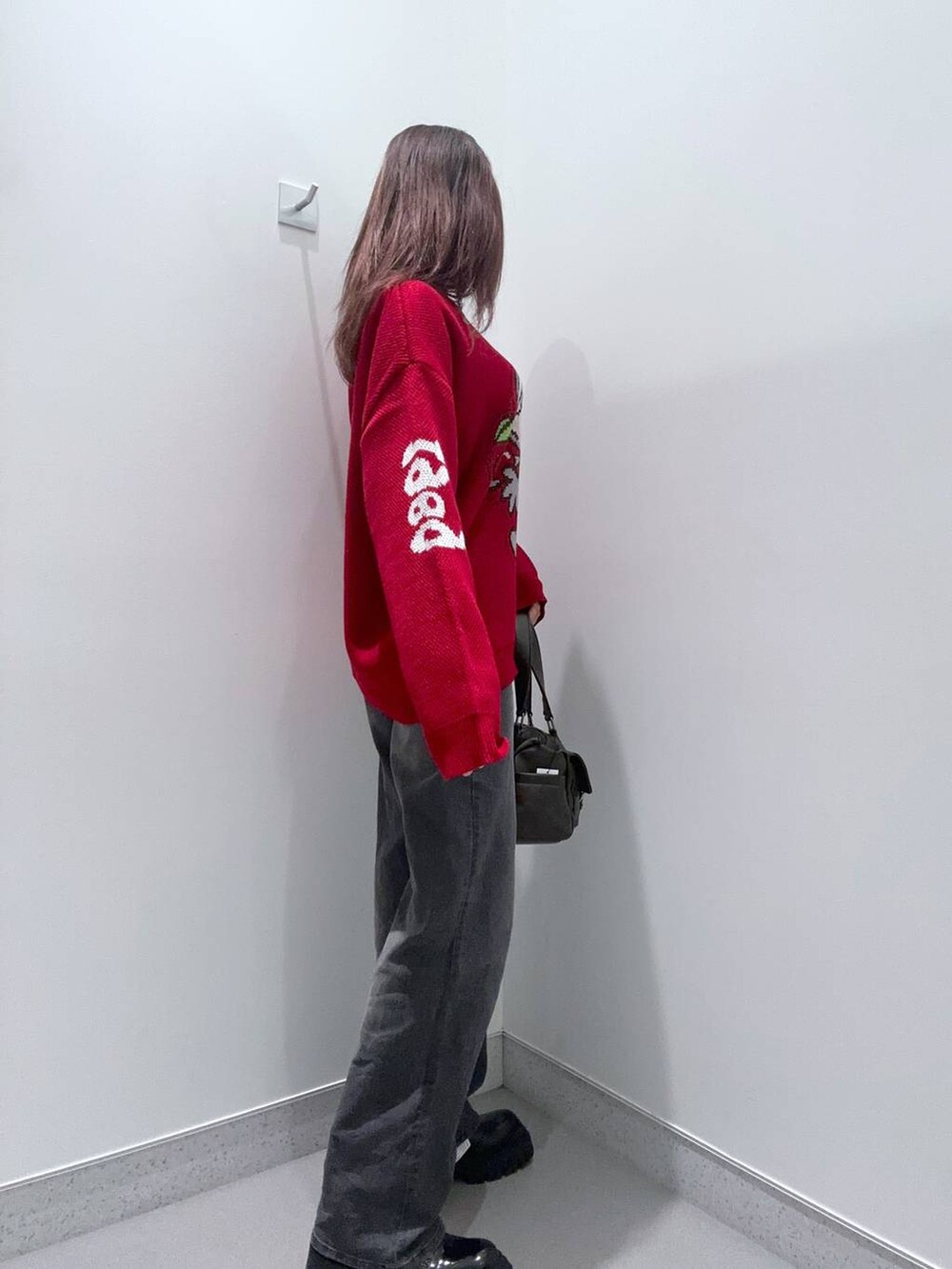 ブラック系のデニムパンツ、ブラウン系のショルダーバッグ、レッド系のニット/セーターを着用したレディースの秋コーディネートの3枚目の写真