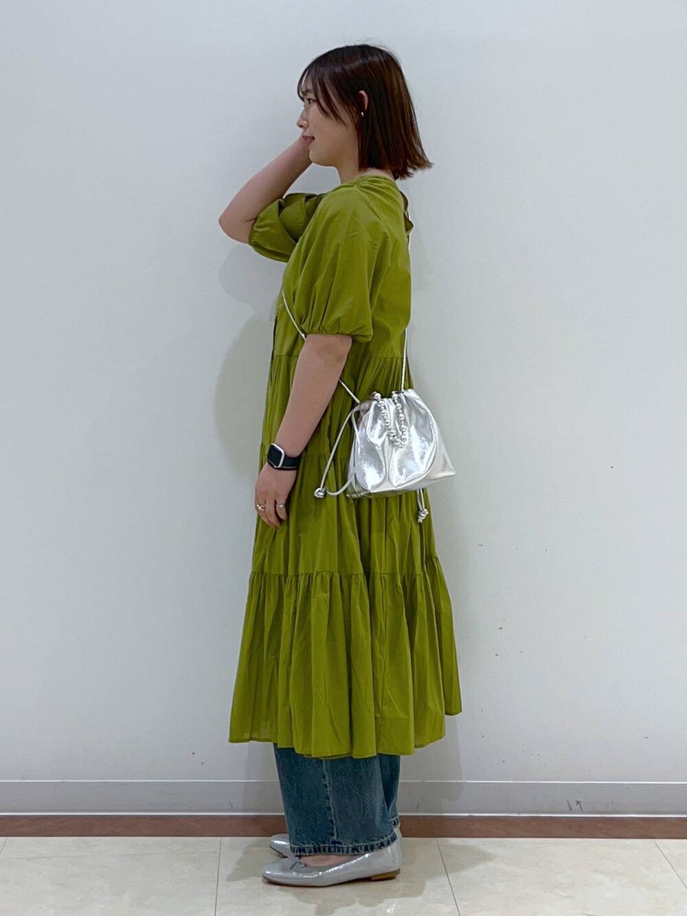 シルバー系のショルダーバッグ、イエロー系のワンピース、ブルー系のデニムパンツを着用したレディースの春コーディネートの2枚目の写真