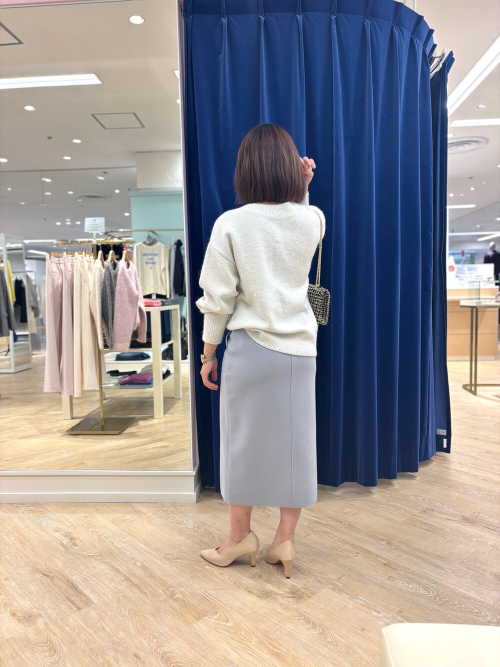 ゴールド系のショルダーバッグ、ブルー系のスカート、ホワイト系のニット/セーターを着用したレディースの冬コーディネートの5枚目の写真