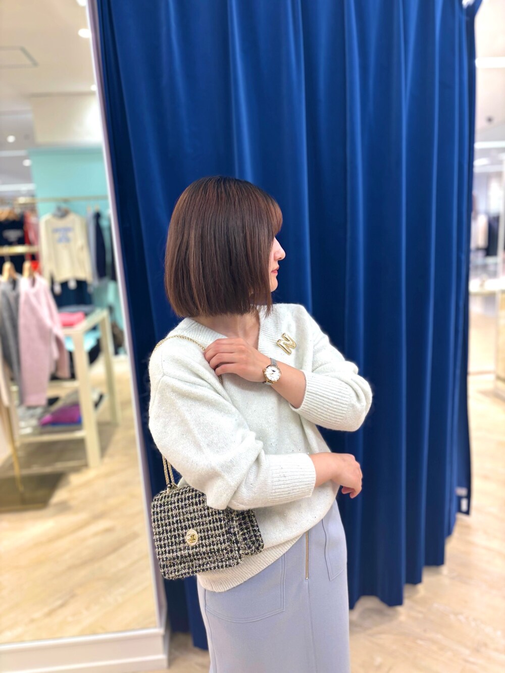 ゴールド系のショルダーバッグ、ブルー系のスカート、ホワイト系のニット/セーターを着用したレディースの冬コーディネートの6枚目の写真