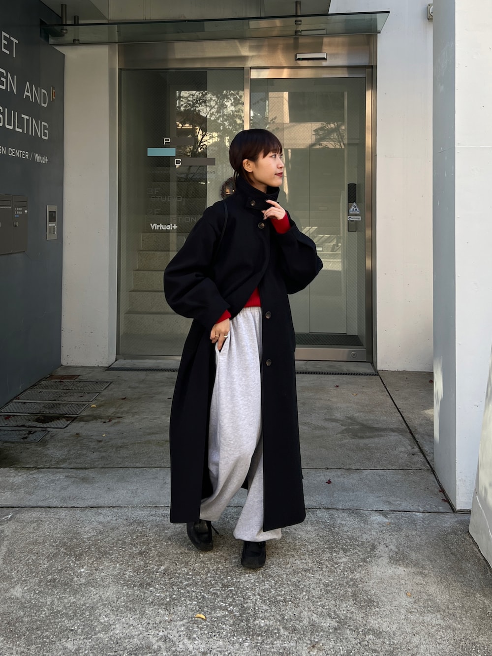 ブラック系のステンカラーコート、レッド系のニット/セーター、グレー系のスウェットパンツを着用したレディースの冬コーディネートの2枚目の写真