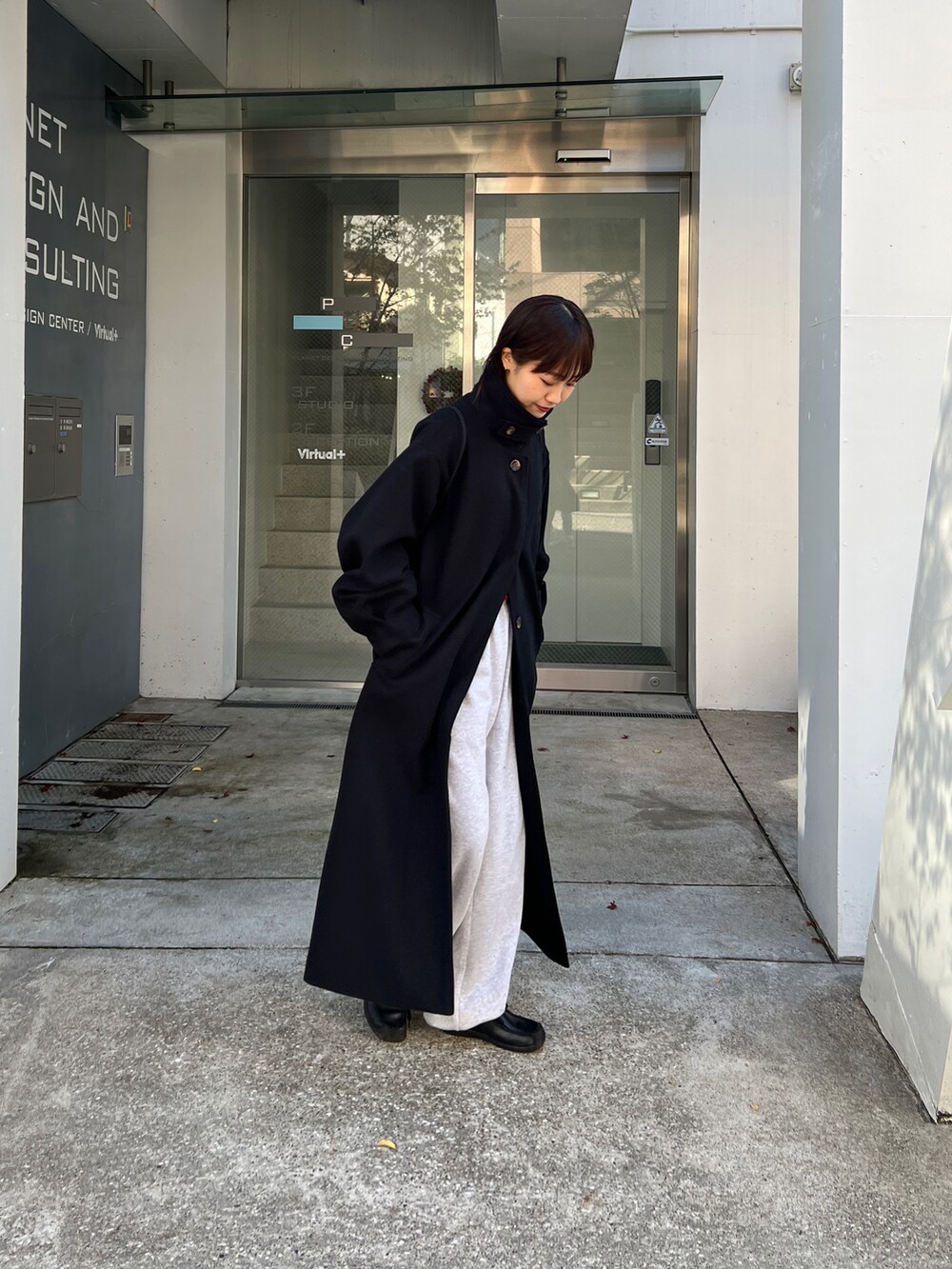 ブラック系のステンカラーコート、レッド系のニット/セーター、グレー系のスウェットパンツを着用したレディースの冬コーディネートの3枚目の写真