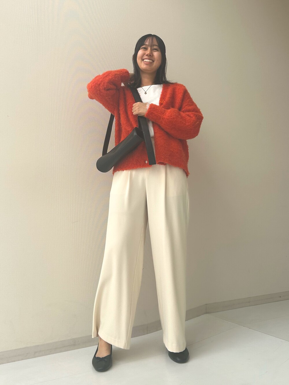 オレンジ系のカーディガン/ボレロ、ベージュ系のスラックス、ブラック系のバレエシューズを着用したレディースの秋コーディネートの2枚目の写真