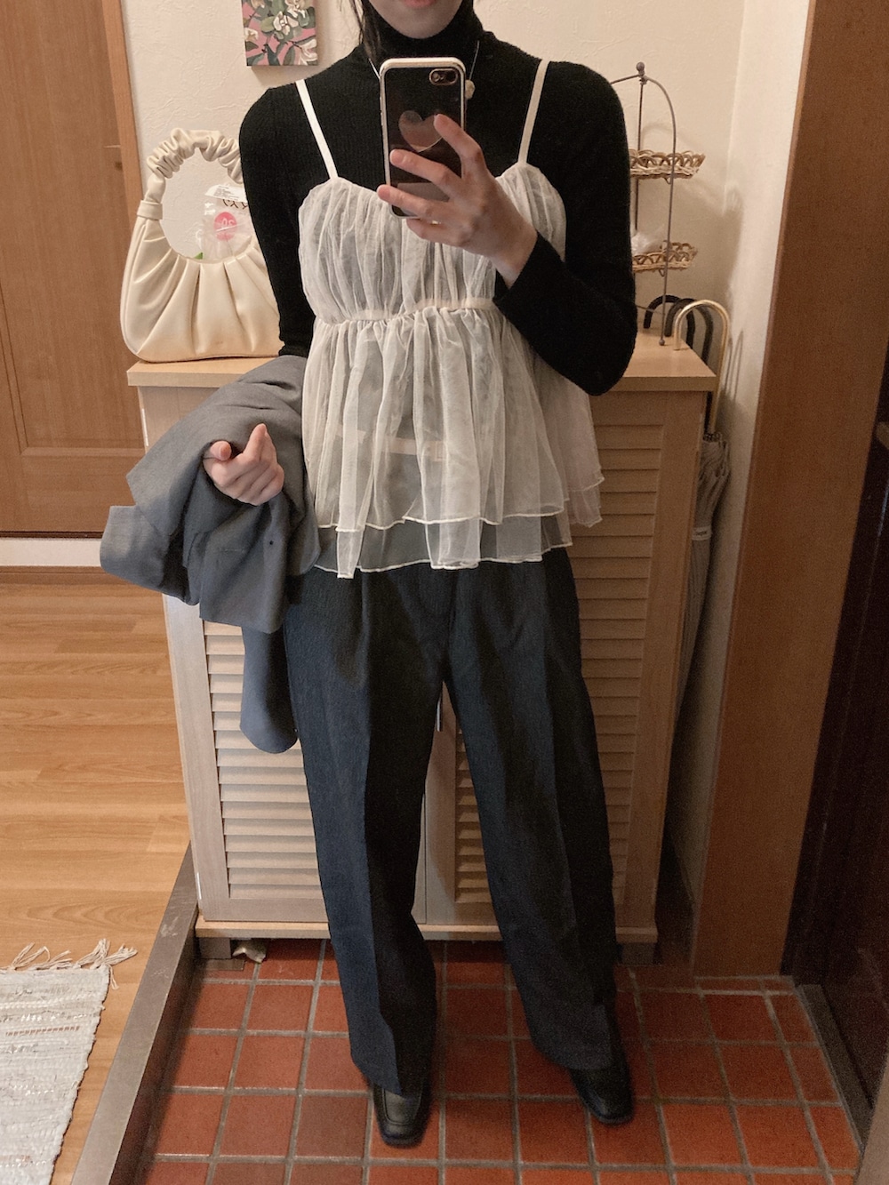 グレー系のスラックス、ホワイト系のハンドバッグ、ブラック系のブーツを着用したレディースの冬コーディネートの2枚目の写真