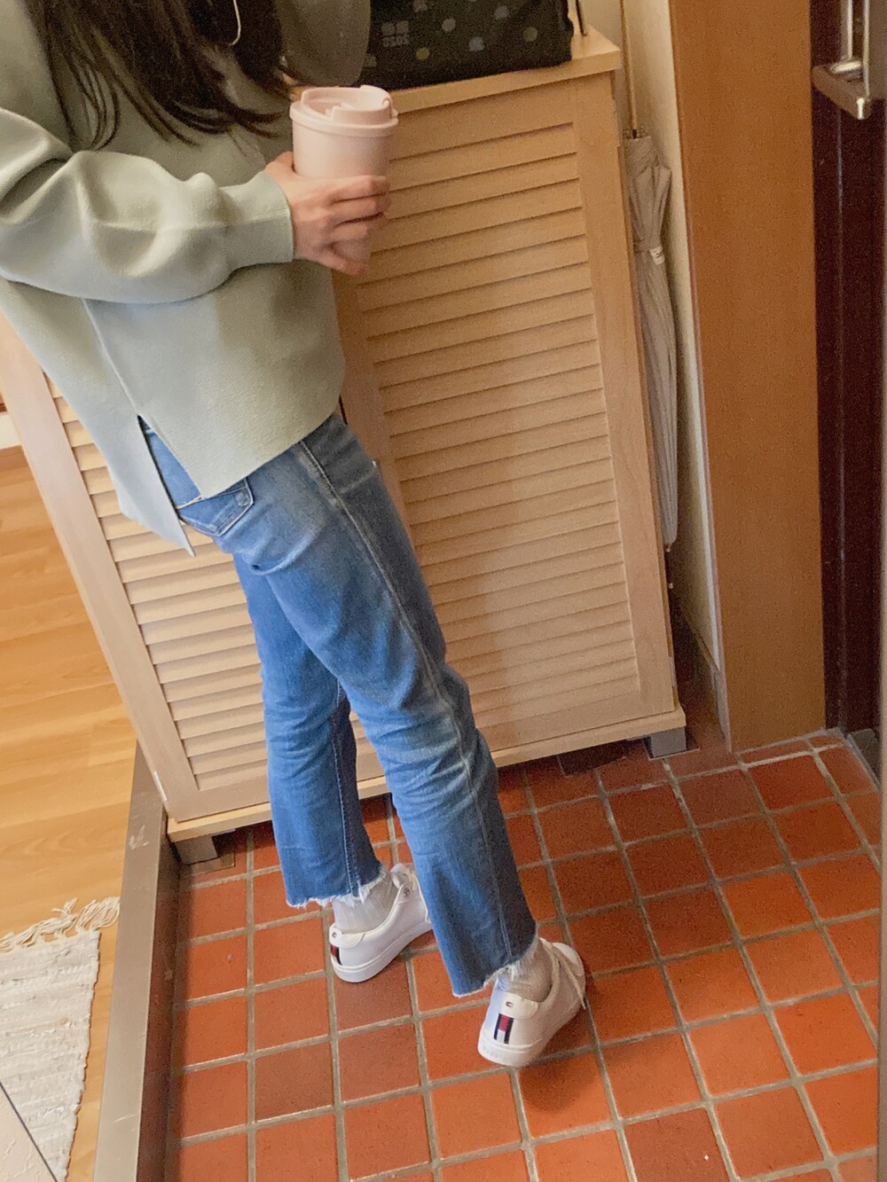 ブルー系のデニムパンツ、グリーン系のトップス、ホワイト系のハンドバッグを着用したレディースの秋コーディネートの2枚目の写真