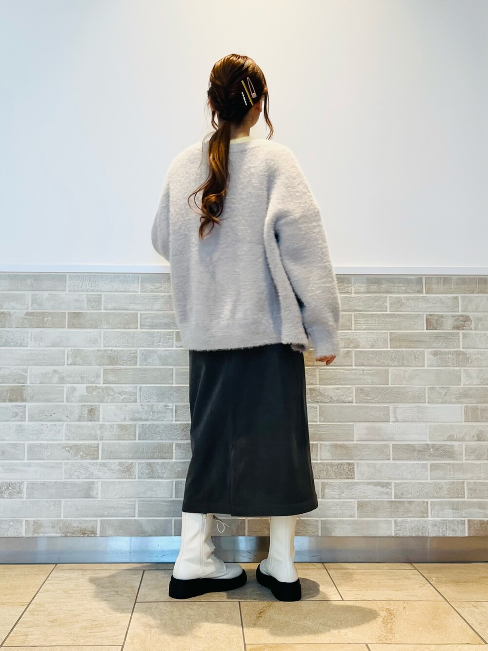 グレー系のスカート、グレー系のカーディガン/ボレロ、イエロー系のニット/セーターを着用したレディースの冬コーディネートの2枚目の写真