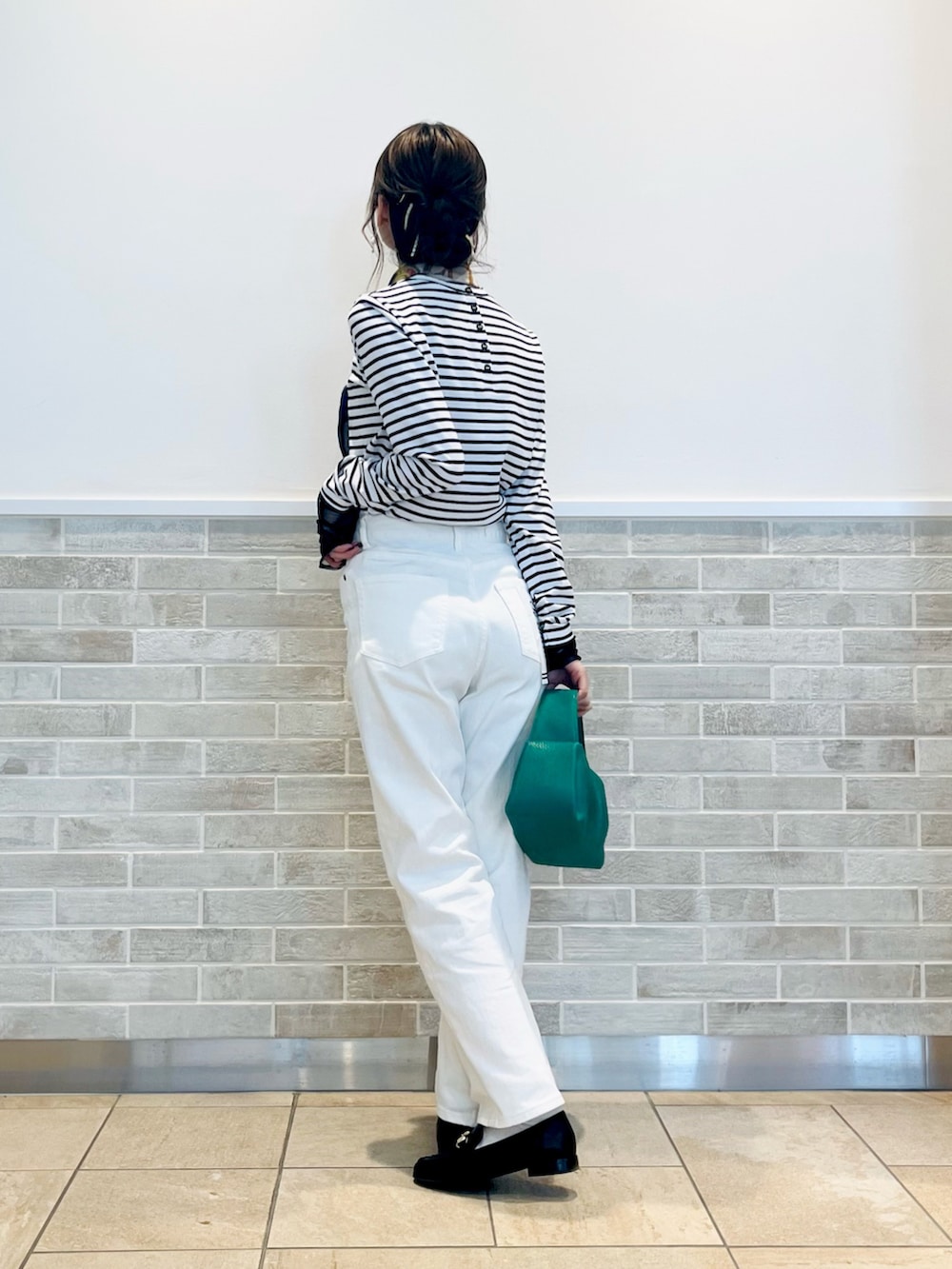 グリーン系のハンドバッグ、ブラック系のTシャツ/カットソー、ホワイト系のデニムパンツを着用したレディースの冬コーディネートの3枚目の写真