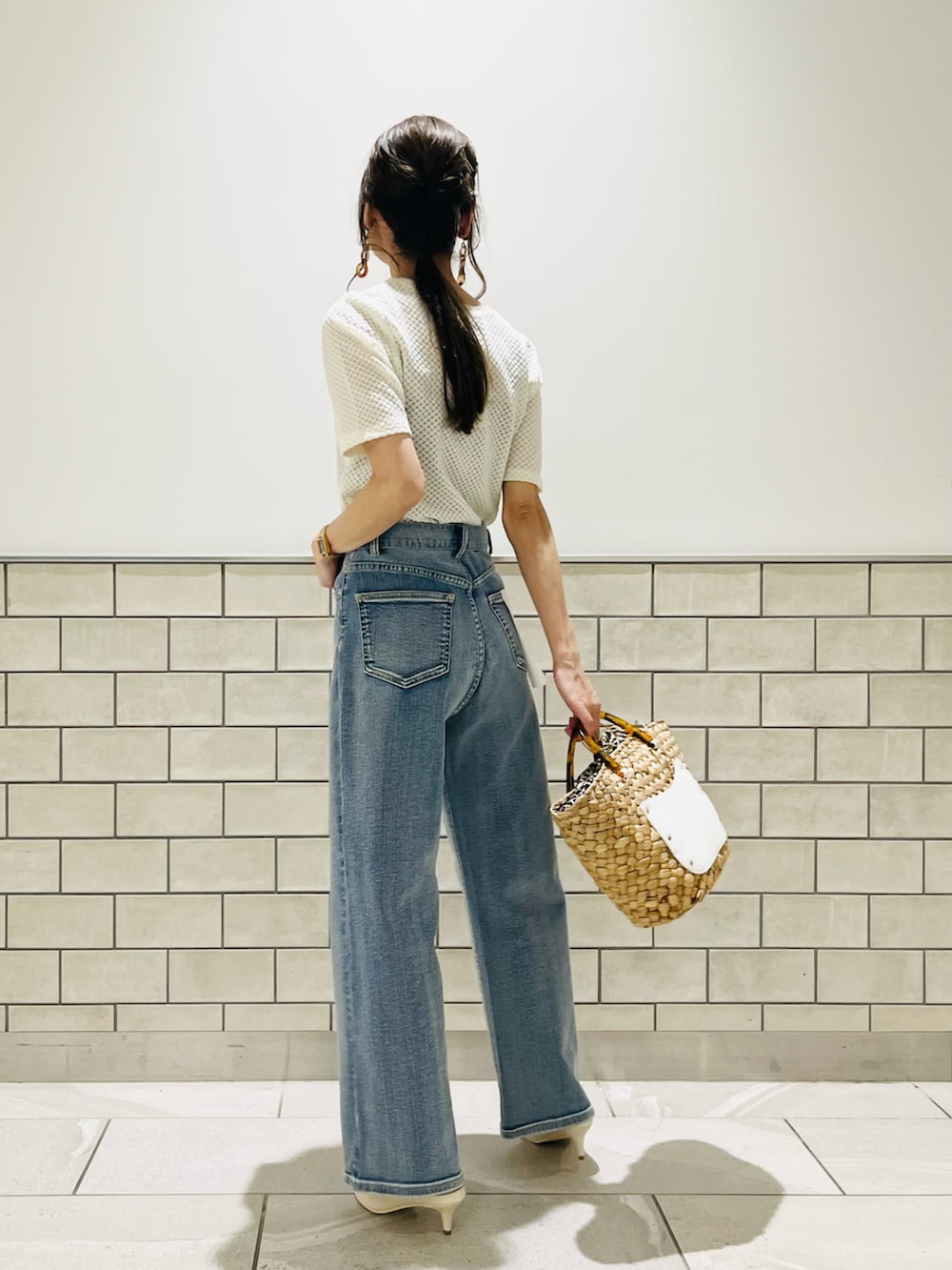 ホワイト系のハンドバッグ、ブルー系のデニムパンツ、ホワイト系のサンダルを着用したレディースの春コーディネートの2枚目の写真