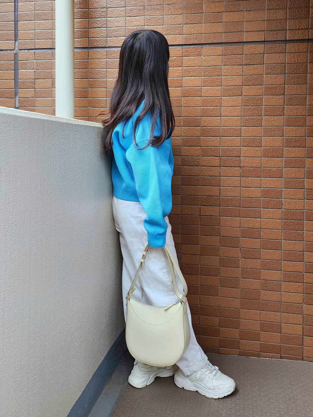 ブルー系のニット/セーター、ホワイト系のデニムパンツ、ホワイト系のスニーカーを着用したレディースの春コーディネートの2枚目の写真