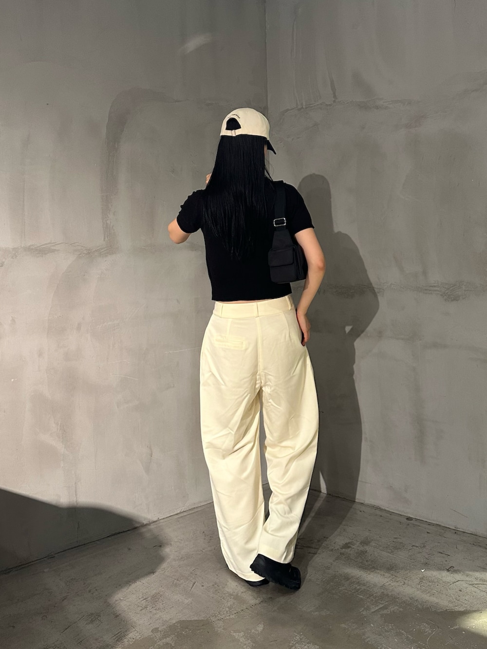 ホワイト系のスラックス、ブラック系のポロシャツ、ブラック系のショルダーバッグを着用したレディースの夏コーディネートの3枚目の写真