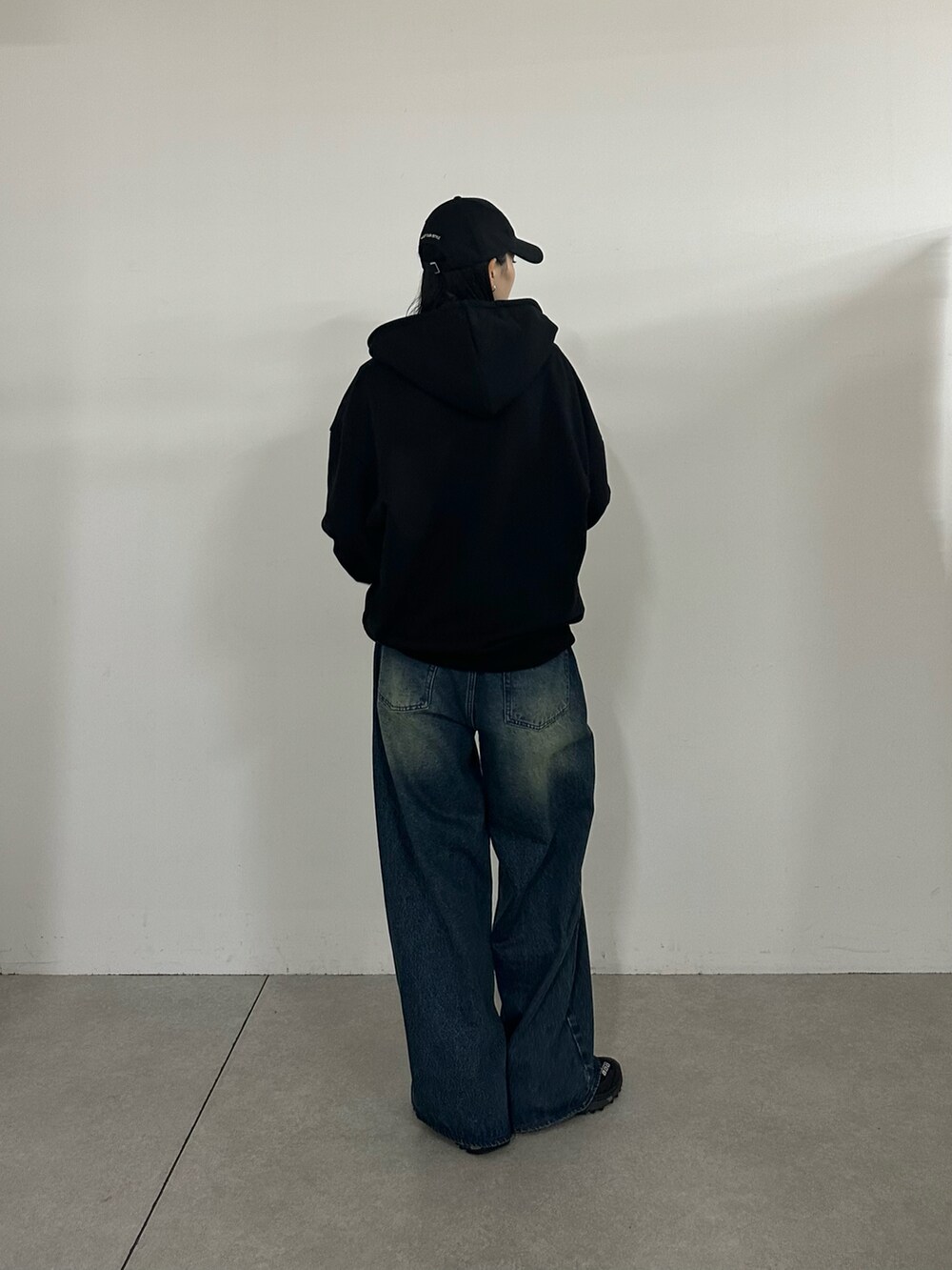 ブラック系のパーカー、ブルー系のデニムパンツ、ブラック系のキャップを着用したレディースの秋コーディネートの3枚目の写真