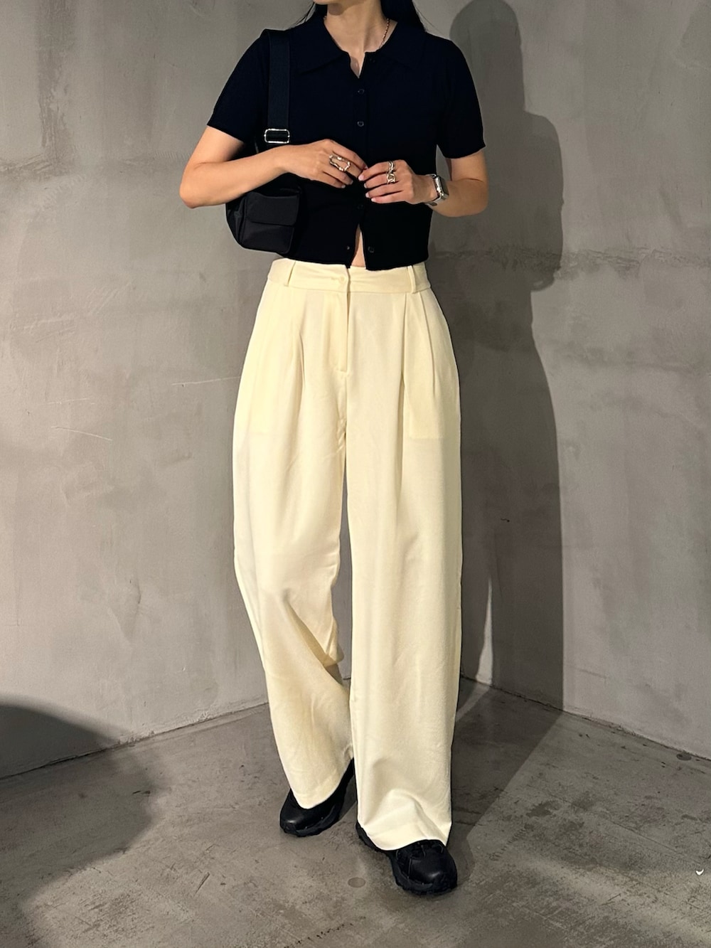 ホワイト系のスラックス、ブラック系のポロシャツ、ブラック系のショルダーバッグを着用したレディースの夏コーディネートの2枚目の写真