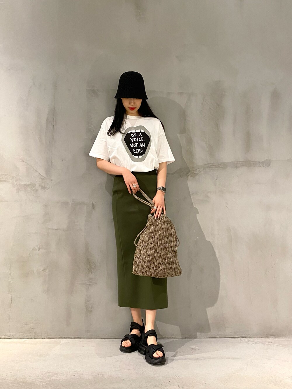 ベージュ系のショルダーバッグ、グリーン系のスカート、ブラック系のハットを着用したレディースの春コーディネートの2枚目の写真