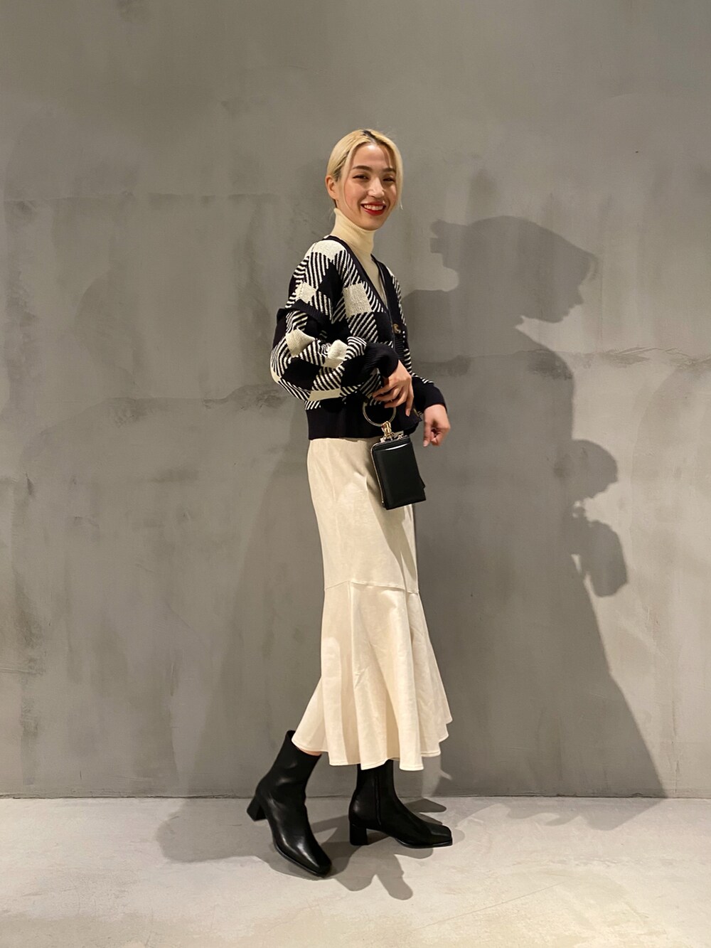 ブラック系のカーディガン/ボレロ、ホワイト系のニット/セーター、ベージュ系のスカートを着用したレディースの冬コーディネートの2枚目の写真