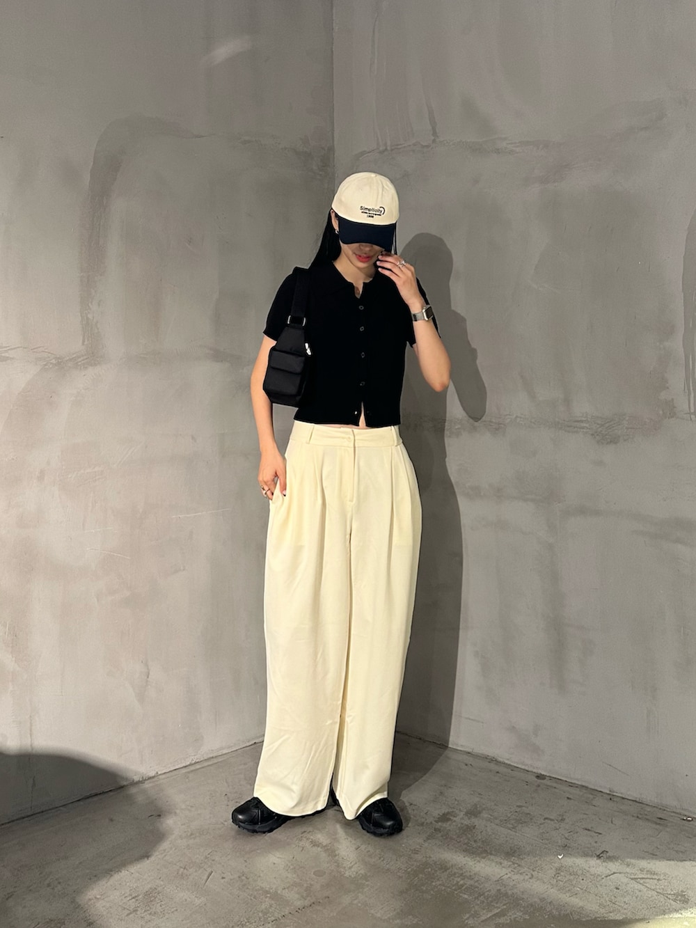 ホワイト系のスラックス、ブラック系のポロシャツ、ブラック系のショルダーバッグを着用したレディースの夏コーディネートの4枚目の写真