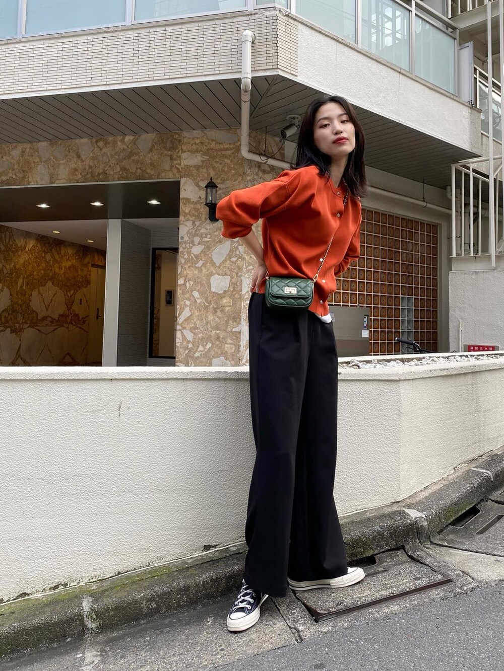 オレンジ系のカーディガン/ボレロ、グリーン系のショルダーバッグ、ブラック系のスラックスを着用したレディースの秋コーディネートの2枚目の写真