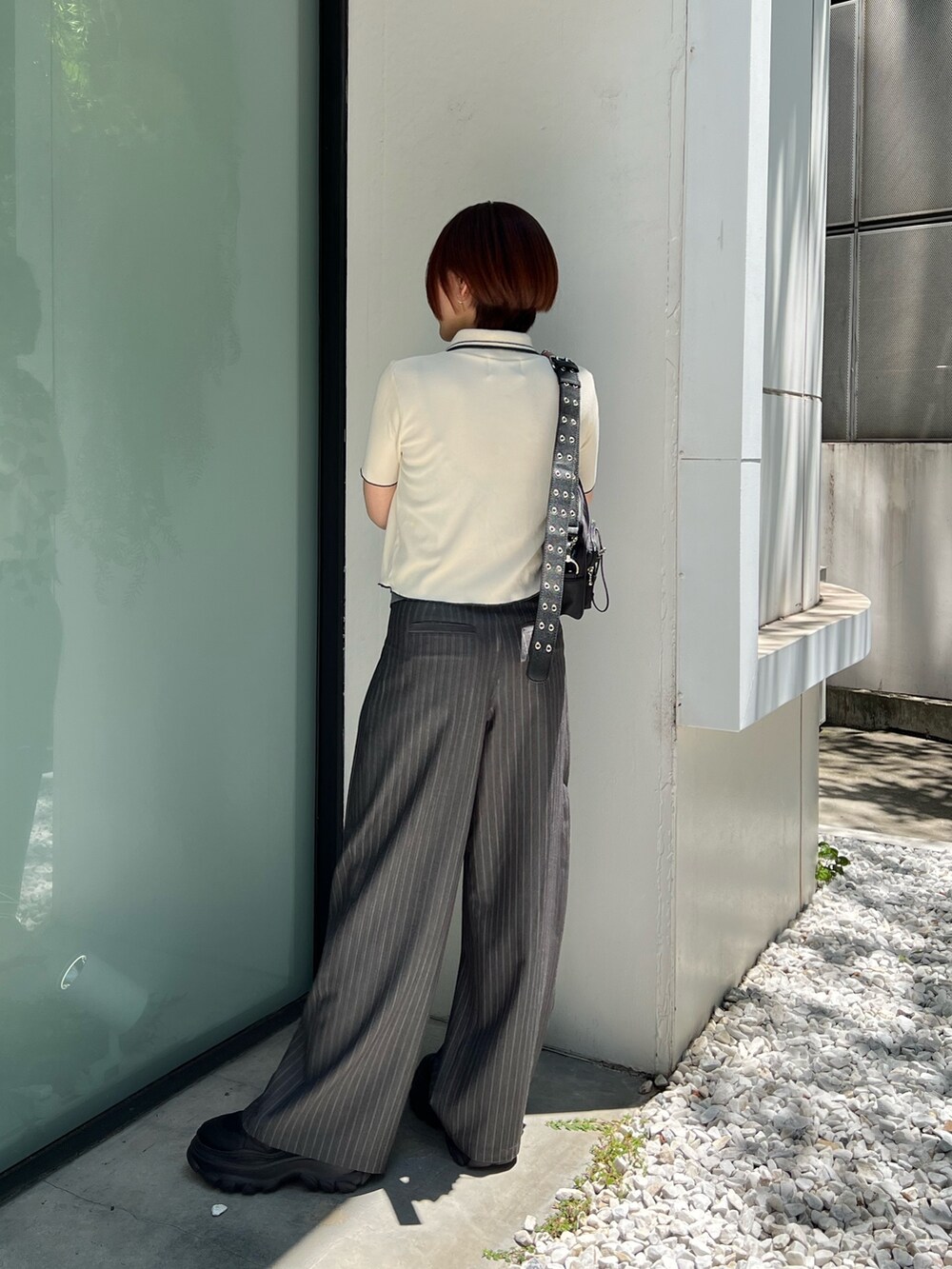 ホワイト系のポロシャツ、グレー系のスラックス、ブラック系のショルダーバッグを着用したレディースの夏コーディネートの3枚目の写真