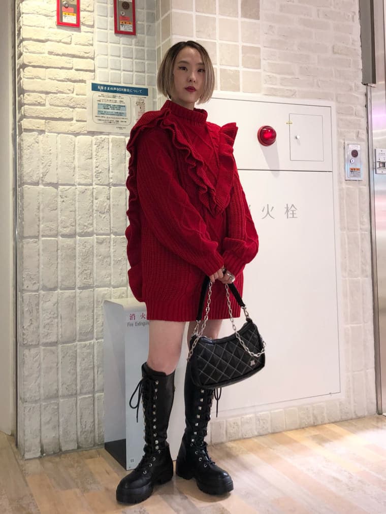 ブラック系のチェスターコート、レッド系のニット/セーター、ブラック系のブーツを着用したレディースの冬コーディネートの4枚目の写真