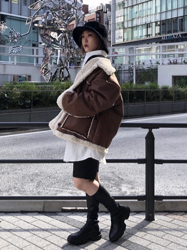 ブラウン系のムートンコート、ブラック系のシャツワンピース、ブラック系のハットを着用したレディースの秋コーディネートの3枚目の写真